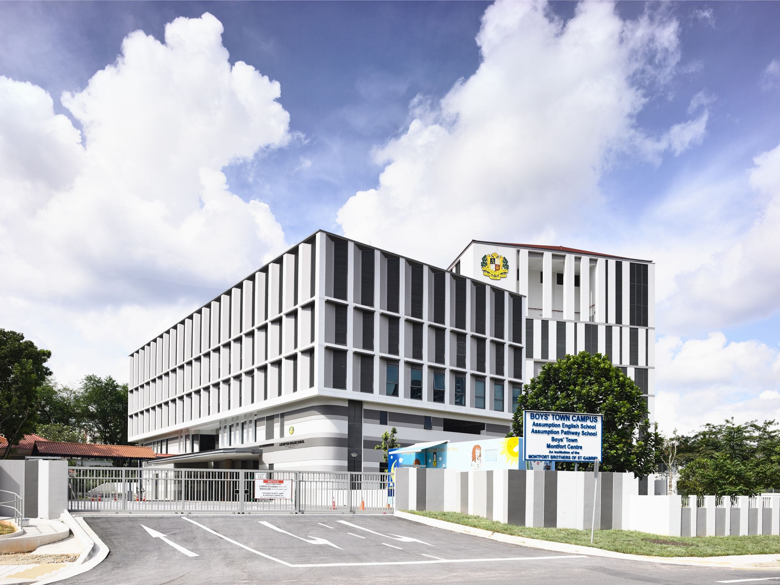 Modern white multi-story Boys' Town Campus building with a blue sign at the entrance gate under a cloudy sky.